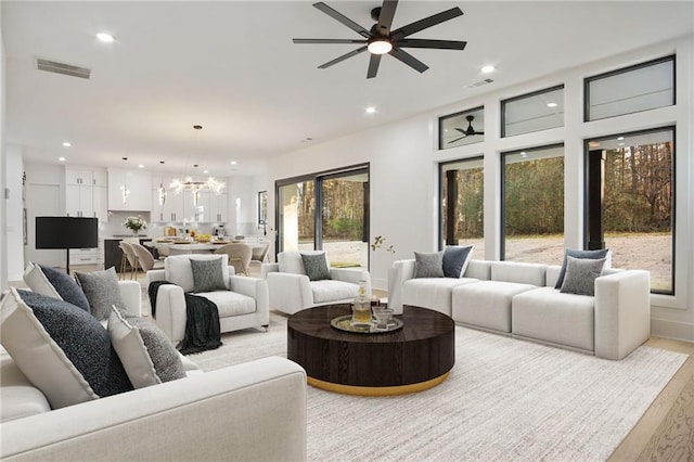 living room with light hardwood / wood-style floors, a healthy amount of sunlight, and ceiling fan with notable chandelier