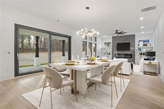 dining room with built in shelves, light wood-type flooring, a fireplace, and ceiling fan with notable chandelier