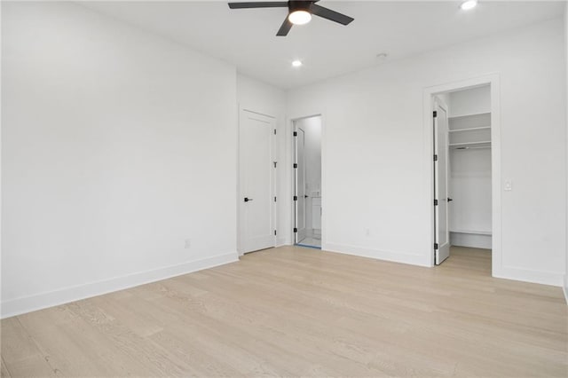 unfurnished bedroom featuring ceiling fan, a walk in closet, a closet, and light hardwood / wood-style flooring