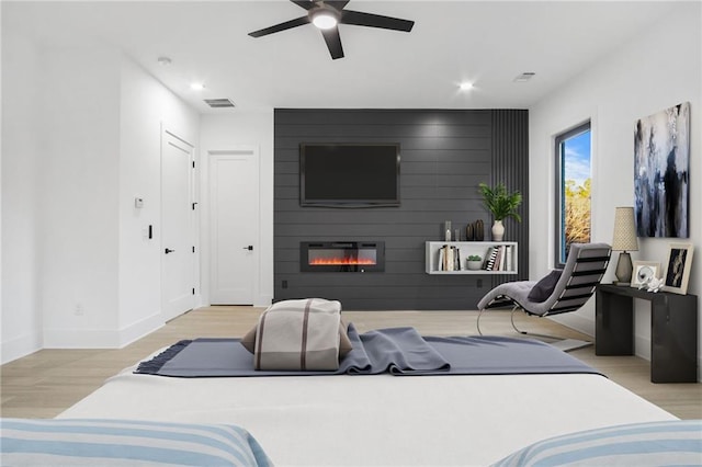 bedroom featuring light wood-type flooring, ceiling fan, and a fireplace