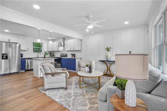 living room featuring crown molding, ceiling fan, sink, and light wood-type flooring