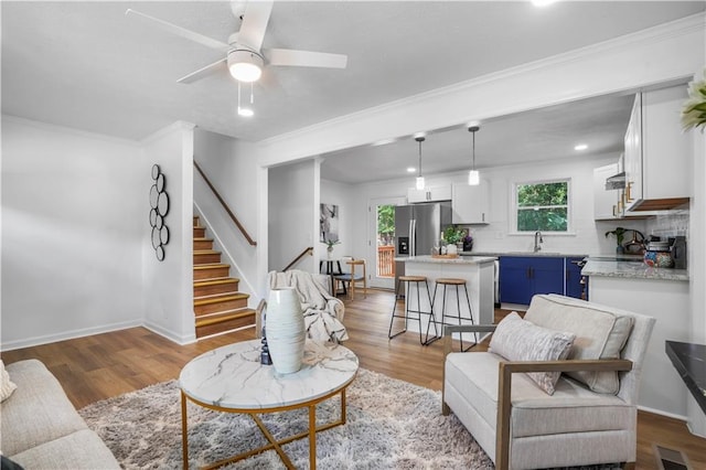 living room with wood-type flooring, ornamental molding, sink, and ceiling fan