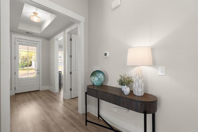 doorway with a tray ceiling, baseboards, visible vents, and light wood finished floors