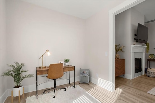 office space featuring a fireplace, baseboards, and wood finished floors