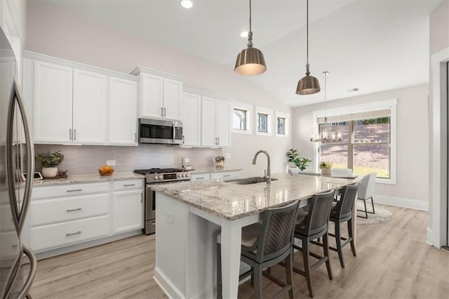 kitchen featuring white cabinets, decorative backsplash, light wood-style flooring, appliances with stainless steel finishes, and a sink