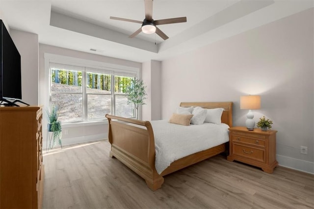 bedroom featuring light wood-type flooring, a tray ceiling, visible vents, and baseboards