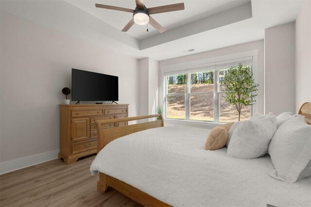 bedroom with a raised ceiling, ceiling fan, and light wood-type flooring