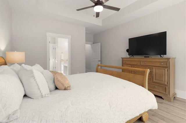 bedroom featuring ceiling fan, baseboards, a tray ceiling, light wood finished floors, and ensuite bath