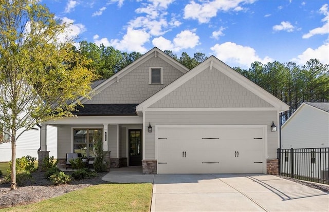 craftsman inspired home featuring a garage, covered porch, fence, concrete driveway, and stone siding