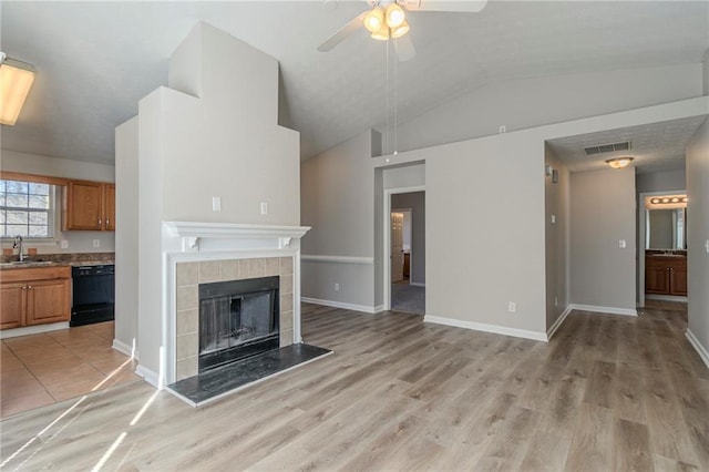 unfurnished living room featuring sink, a fireplace, vaulted ceiling, and light wood-type flooring