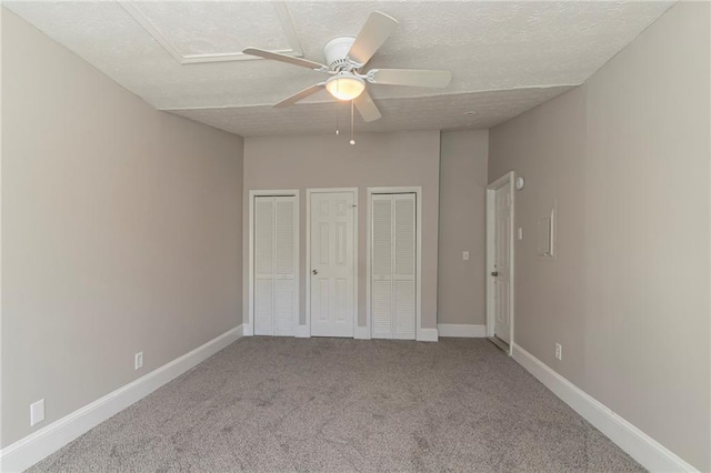 unfurnished bedroom featuring multiple closets, ceiling fan, carpet floors, and a textured ceiling