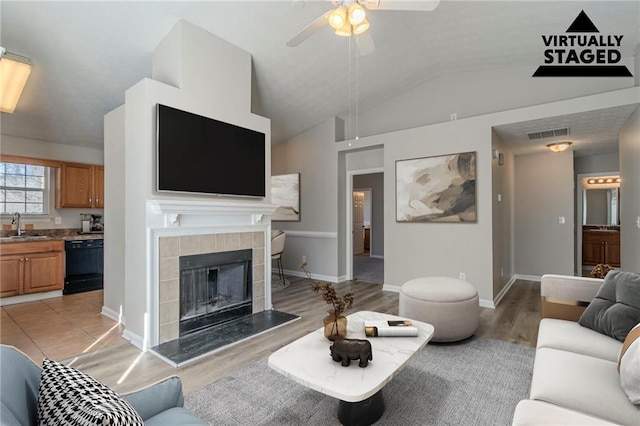 living room with lofted ceiling, sink, light hardwood / wood-style flooring, ceiling fan, and a fireplace