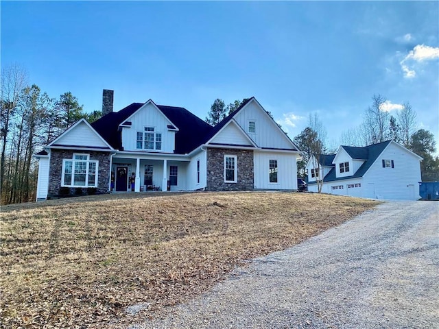 modern farmhouse style home featuring a chimney, a porch, board and batten siding, stone siding, and a front lawn