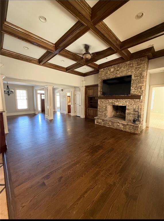 unfurnished living room featuring dark wood finished floors, a fireplace, coffered ceiling, beamed ceiling, and ceiling fan with notable chandelier