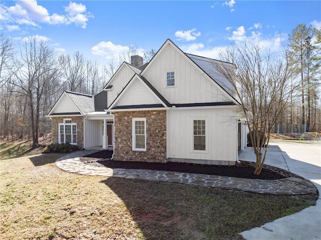 view of front of house featuring stone siding, driveway, board and batten siding, and a chimney