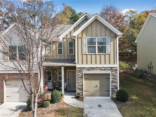 view of front of home featuring an attached garage, driveway, stone siding, a front lawn, and board and batten siding