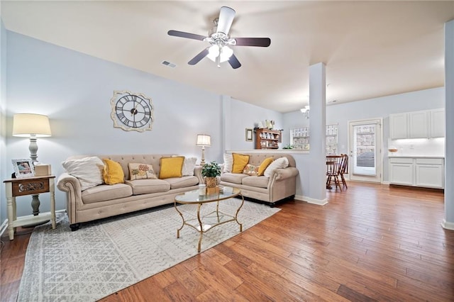 living area with baseboards, wood finished floors, visible vents, and a ceiling fan