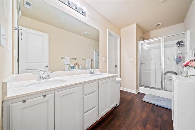 bathroom featuring double vanity, visible vents, wood finished floors, a shower stall, and a sink