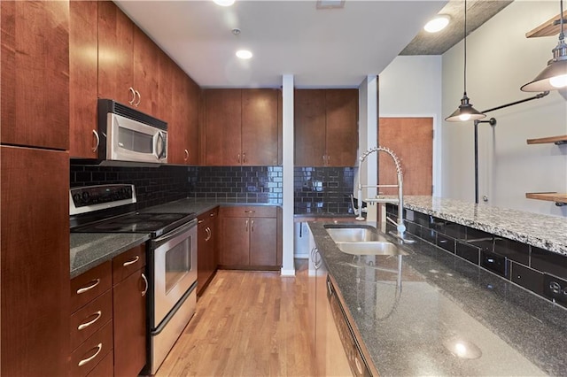 kitchen with stainless steel appliances, a sink, light wood-style flooring, tasteful backsplash, and dark stone countertops