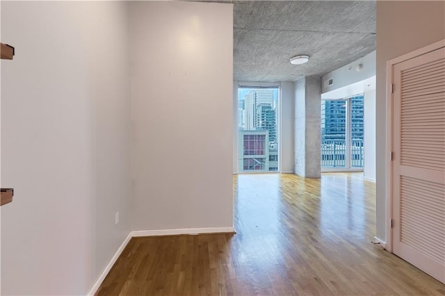 hallway with wood finished floors, a wall of windows, and baseboards