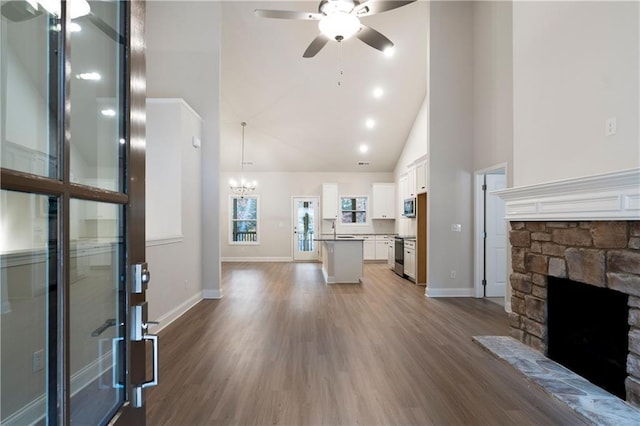 unfurnished living room with a stone fireplace, high vaulted ceiling, ceiling fan with notable chandelier, and hardwood / wood-style flooring