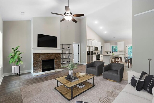 living room featuring high vaulted ceiling, sink, ceiling fan, light wood-type flooring, and a fireplace