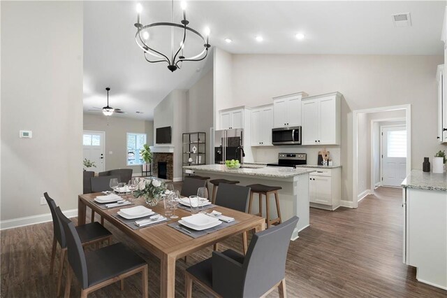 dining area with ceiling fan with notable chandelier, dark hardwood / wood-style floors, a stone fireplace, and a wealth of natural light