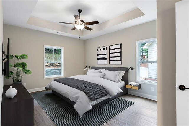 bedroom featuring hardwood / wood-style flooring, a raised ceiling, and multiple windows