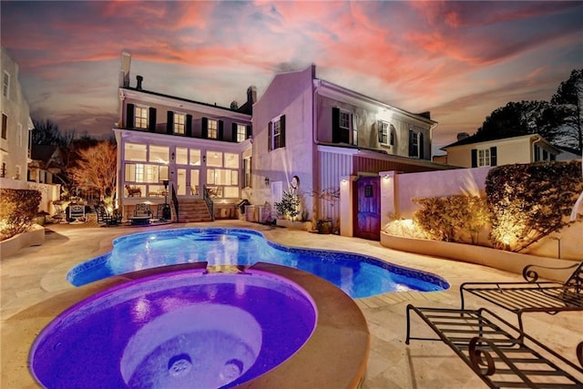 pool at dusk featuring an in ground hot tub and a patio