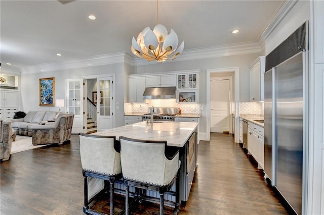 kitchen featuring built in refrigerator, hanging light fixtures, a center island with sink, and white cabinets