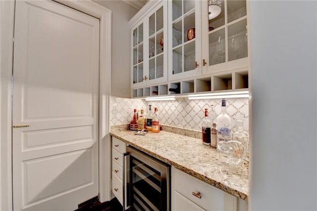 bar featuring wine cooler, light stone counters, white cabinetry, and tasteful backsplash