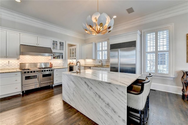 kitchen with decorative light fixtures, white cabinetry, sink, high end appliances, and light stone counters