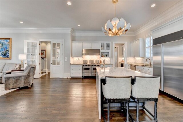 kitchen with sink, white cabinetry, decorative light fixtures, a center island with sink, and premium appliances