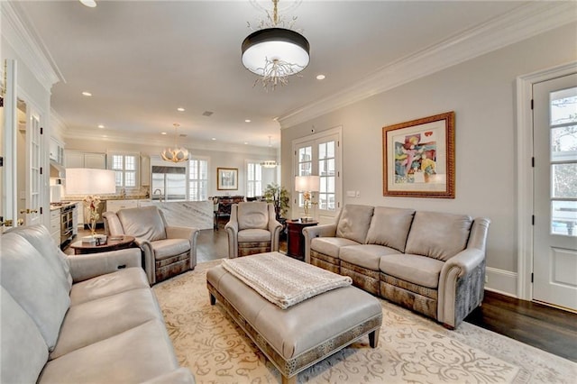 living room featuring an inviting chandelier, ornamental molding, light wood-type flooring, and a wealth of natural light