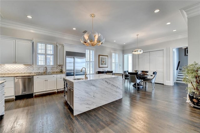 kitchen with pendant lighting, sink, appliances with stainless steel finishes, white cabinetry, and a center island with sink