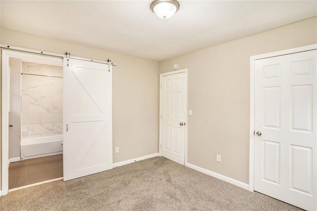 unfurnished bedroom featuring a barn door, baseboards, carpet, and connected bathroom