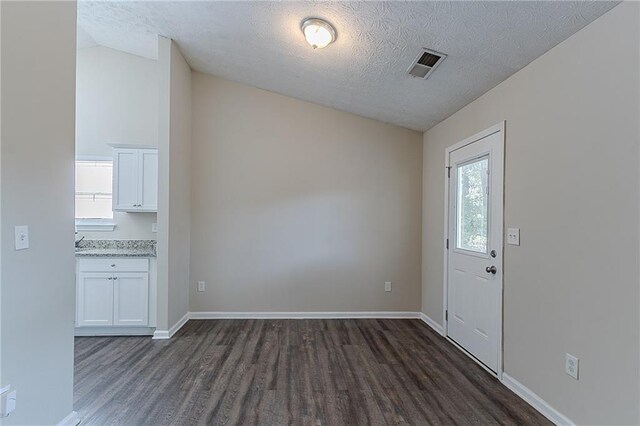 unfurnished dining area featuring dark wood-type flooring, healthy amount of natural light, a textured ceiling, lofted ceiling, and baseboards