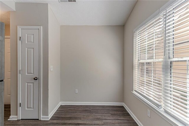 unfurnished room featuring plenty of natural light, dark wood-type flooring, and baseboards