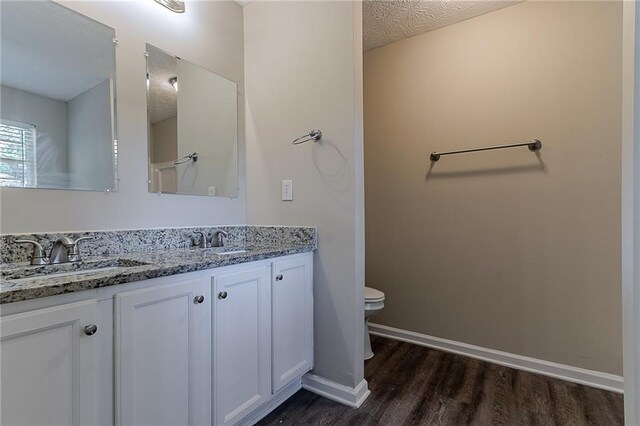 full bath with wood finished floors, toilet, double vanity, and baseboards