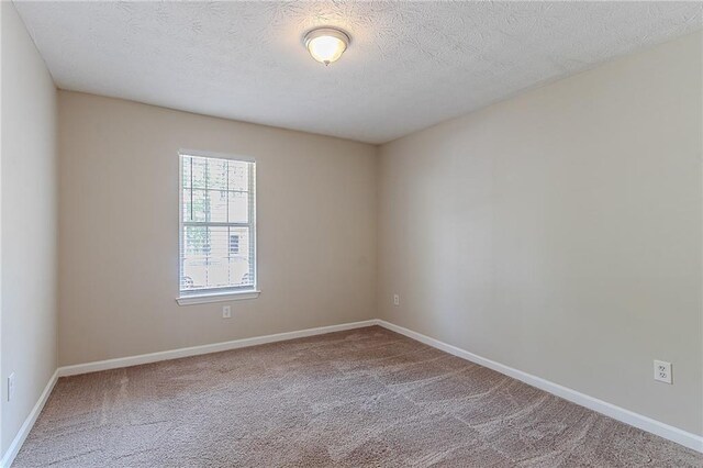 empty room with carpet floors, baseboards, and a textured ceiling
