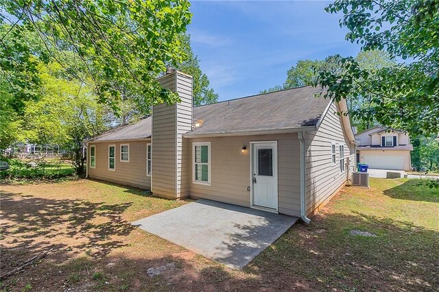 back of property with a chimney, a patio area, central air condition unit, a lawn, and a shingled roof