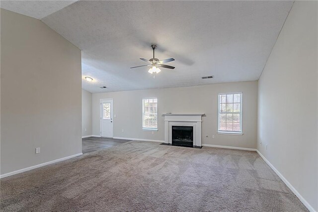 unfurnished living room featuring ceiling fan, carpet flooring, baseboards, a fireplace with flush hearth, and a textured ceiling