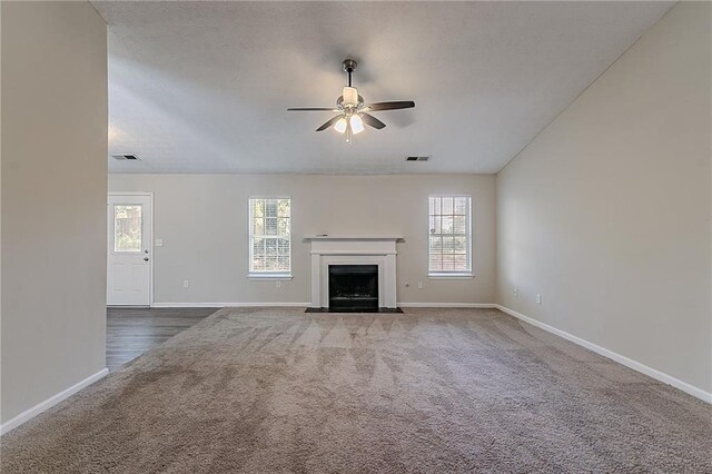 unfurnished living room with carpet floors, a ceiling fan, baseboards, and a fireplace with flush hearth