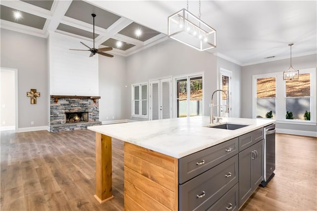 kitchen with light stone countertops, sink, coffered ceiling, a stone fireplace, and beamed ceiling