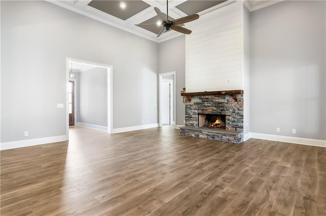 unfurnished living room with a high ceiling, coffered ceiling, a stone fireplace, ceiling fan, and beamed ceiling