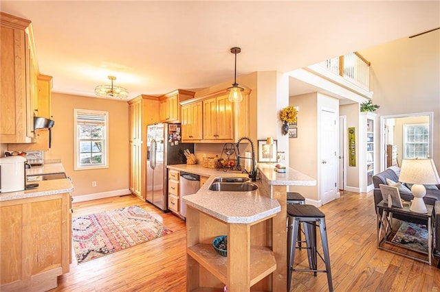 kitchen featuring light wood finished floors, a kitchen bar, a peninsula, stainless steel appliances, and a sink