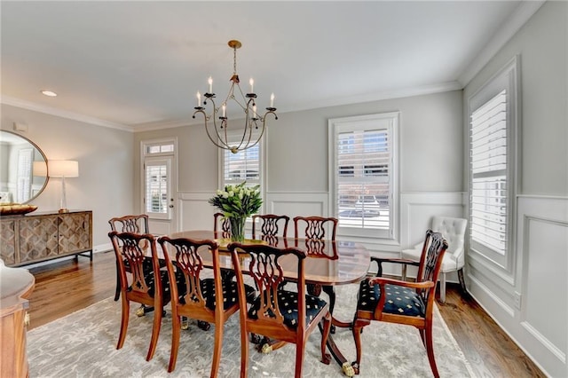 dining area with a wainscoted wall, wood finished floors, crown molding, a chandelier, and a decorative wall