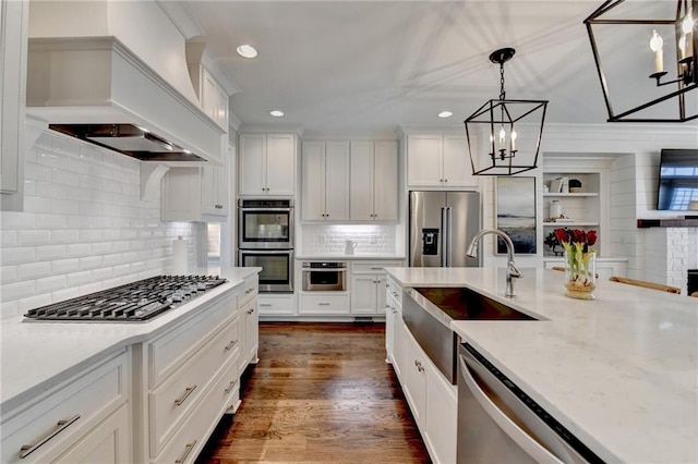 kitchen with a sink, white cabinets, appliances with stainless steel finishes, custom exhaust hood, and decorative light fixtures