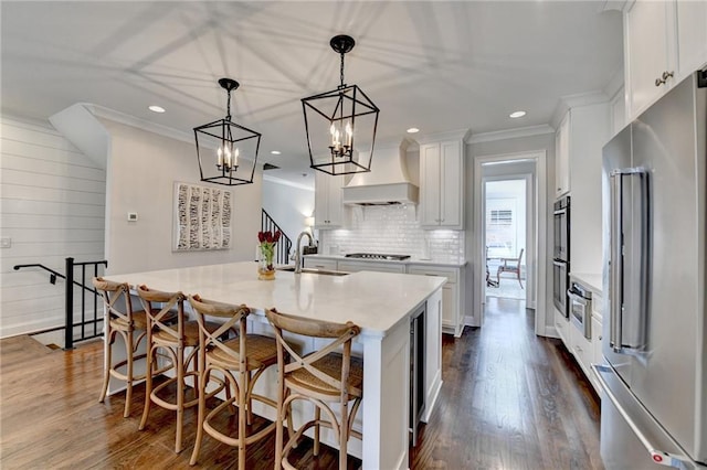 kitchen featuring dark wood finished floors, high end fridge, stovetop, premium range hood, and a sink