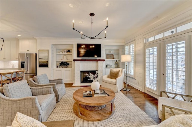 living room with a fireplace with flush hearth, crown molding, an inviting chandelier, and wood finished floors